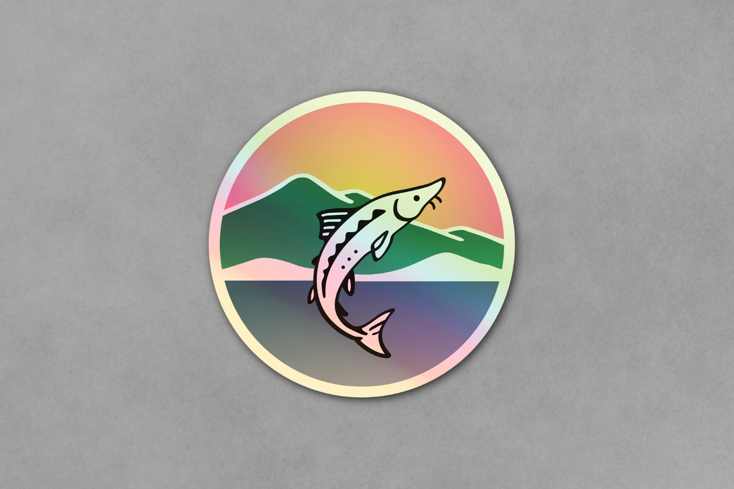 Round sticker with a sturgeon and mountain design on a gray background.